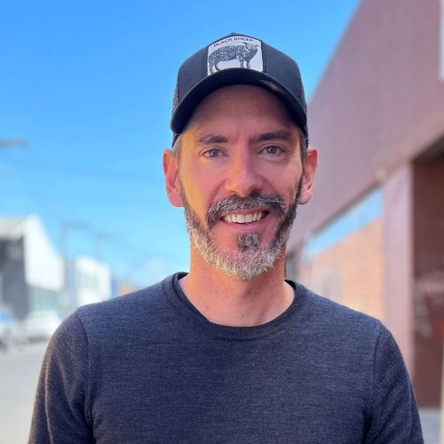 Man wearing a black cap with a logo and dark shirt outdoors